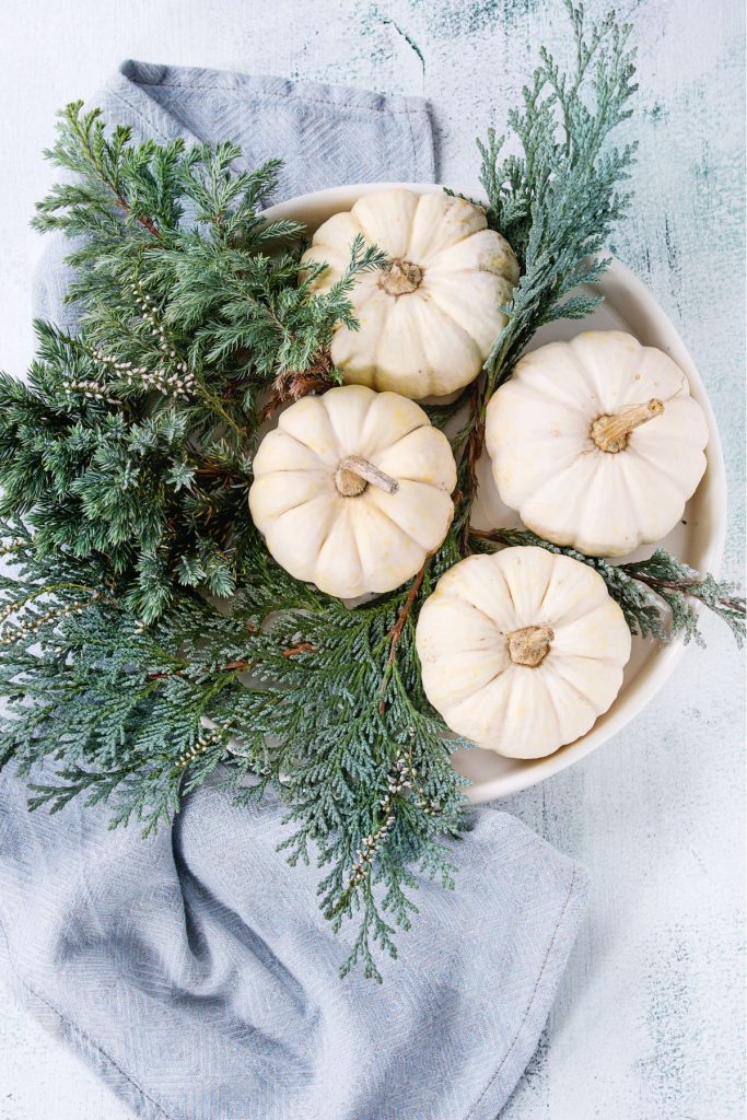 a bowl with four white mini faux pumpkins and some greenery