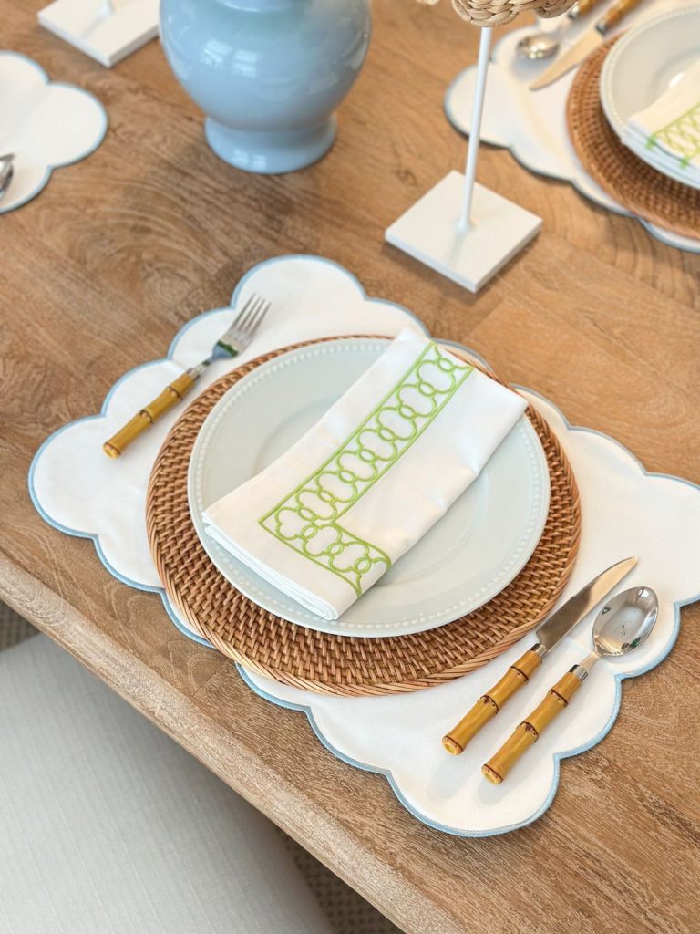a scalloped placemat with a rattan charger, white dinner plates, a cloth napkin, and bamboo silverware
